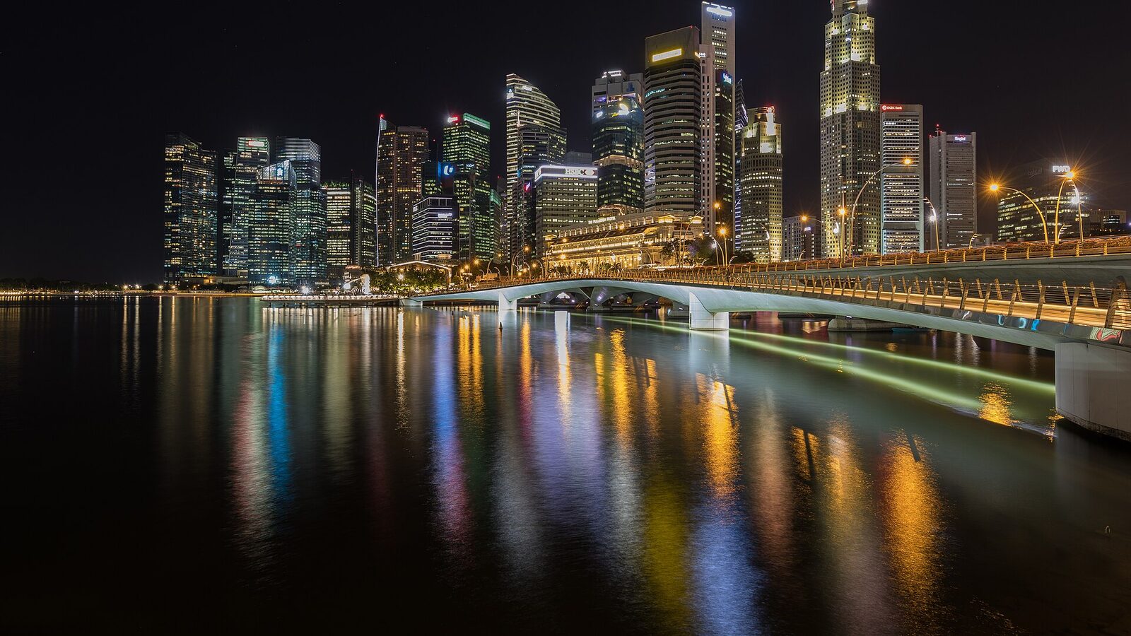 Skyline of the Central Business District of Singapore with the Esplanade Bridge at night, and colorful lights reflected in the water