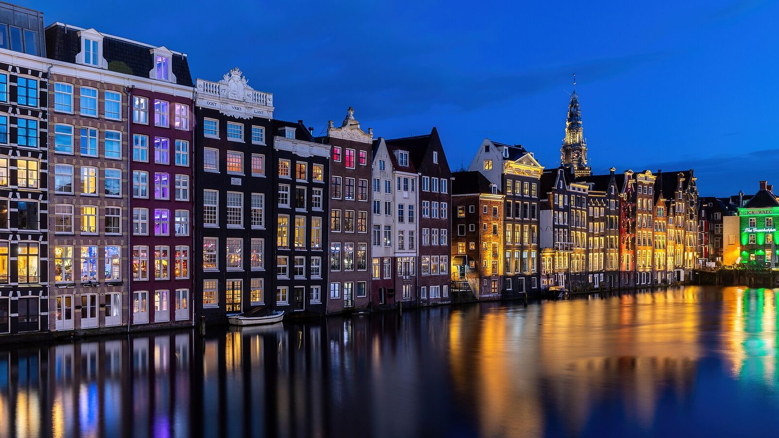 Colorful windows and canal houses at blue hour with water reflection in Damrak Amsterdam Netherlands